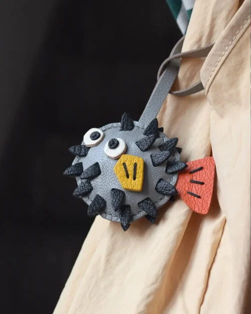 A whimsical pufferfish bag charm handcrafted from French goatskin leather. Hand-stitched over three days and gift boxed for bags, keys, or car keys.