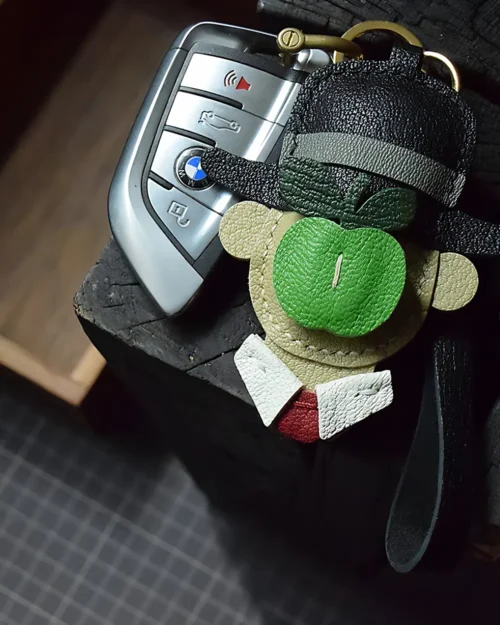 A surreal apple gentleman bag charm handcrafted from premium leather. Hand-stitched over three days and gift boxed for bags, keys, or car keys.