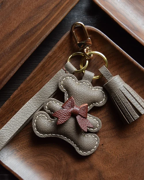 A playful bow bear bag charm handcrafted from French goatskin leather. Hand-stitched over three days and gift boxed for bags, keys, or car keys.