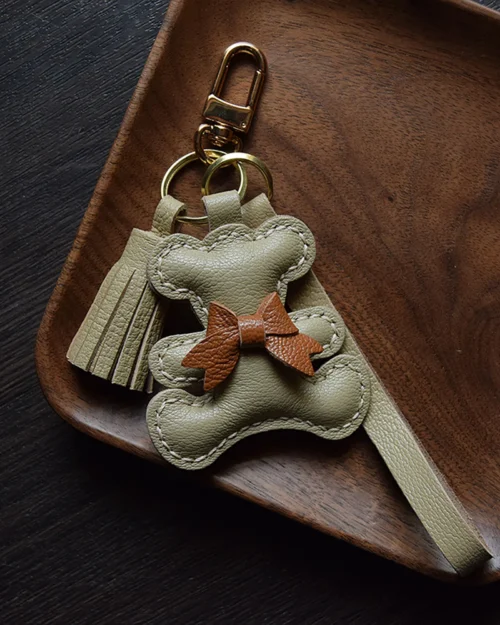 A playful bow bear bag charm handcrafted from French goatskin leather. Hand-stitched over three days and gift boxed for bags, keys, or car keys.