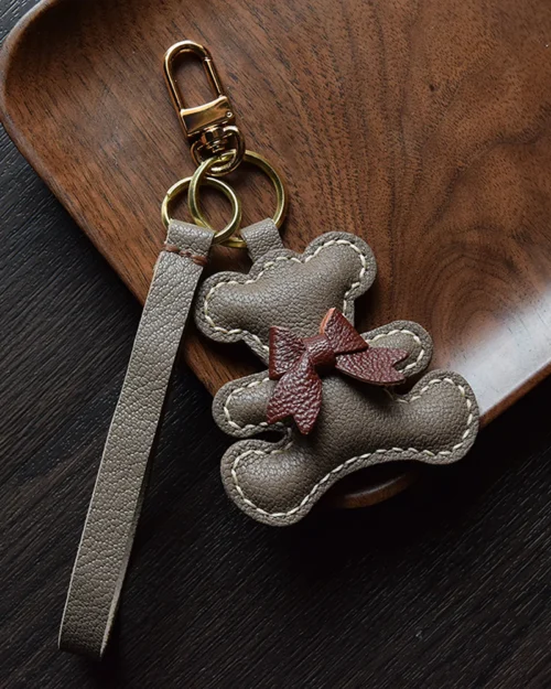 A playful bow bear bag charm handcrafted from French goatskin leather. Hand-stitched over three days and gift boxed for bags, keys, or car keys.