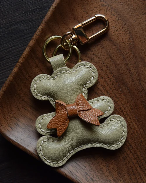 A playful bow bear bag charm handcrafted from French goatskin leather. Hand-stitched over three days and gift boxed for bags, keys, or car keys.