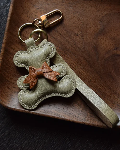 A playful bow bear bag charm handcrafted from French goatskin leather. Hand-stitched over three days and gift boxed for bags, keys, or car keys.