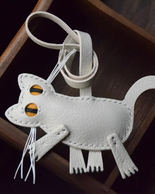 A playful cat bag charm handcrafted from French goatskin leather. Hand-stitched over three days and gift boxed for bags, keys, or car keys.