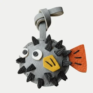 A whimsical pufferfish bag charm handcrafted from French goatskin leather. Hand-stitched over three days and gift boxed for bags, keys, or car keys.