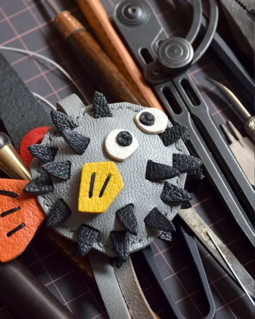 A whimsical pufferfish bag charm handcrafted from French goatskin leather. Hand-stitched over three days and gift boxed for bags, keys, or car keys.