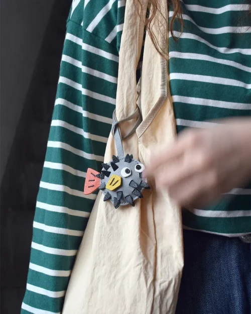 A whimsical pufferfish bag charm handcrafted from French goatskin leather. Hand-stitched over three days and gift boxed for bags, keys, or car keys.