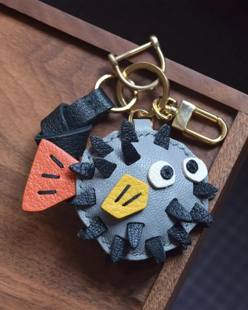 A whimsical pufferfish bag charm handcrafted from French goatskin leather. Hand-stitched over three days and gift boxed for bags, keys, or car keys.